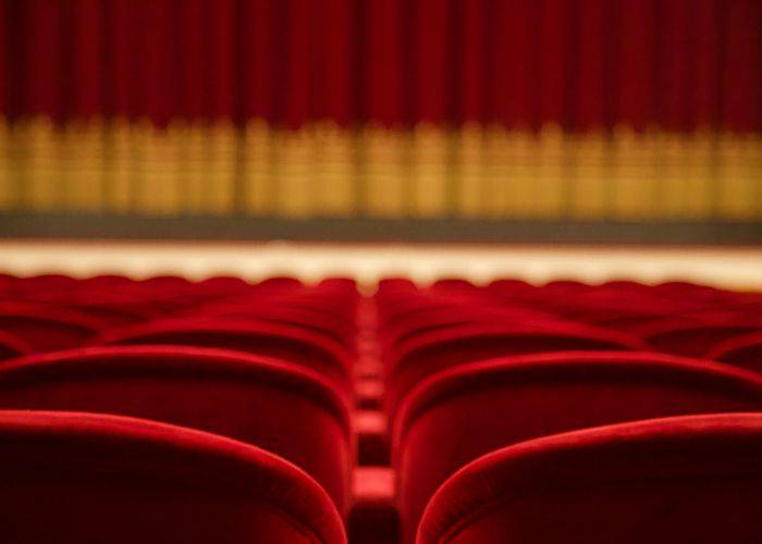 Velvet red seats at a theater. The curtain is still closed and the seats are empty.